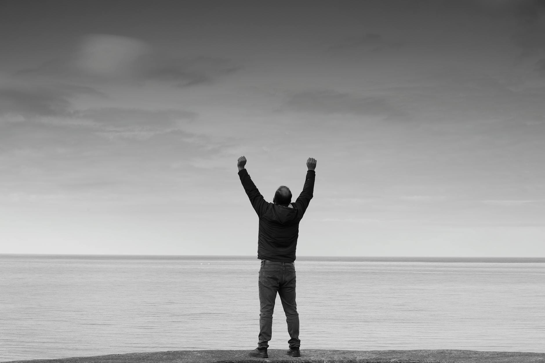 Człowiek z uniesionymi rękami nad morzem w czarno-białej tonacji
