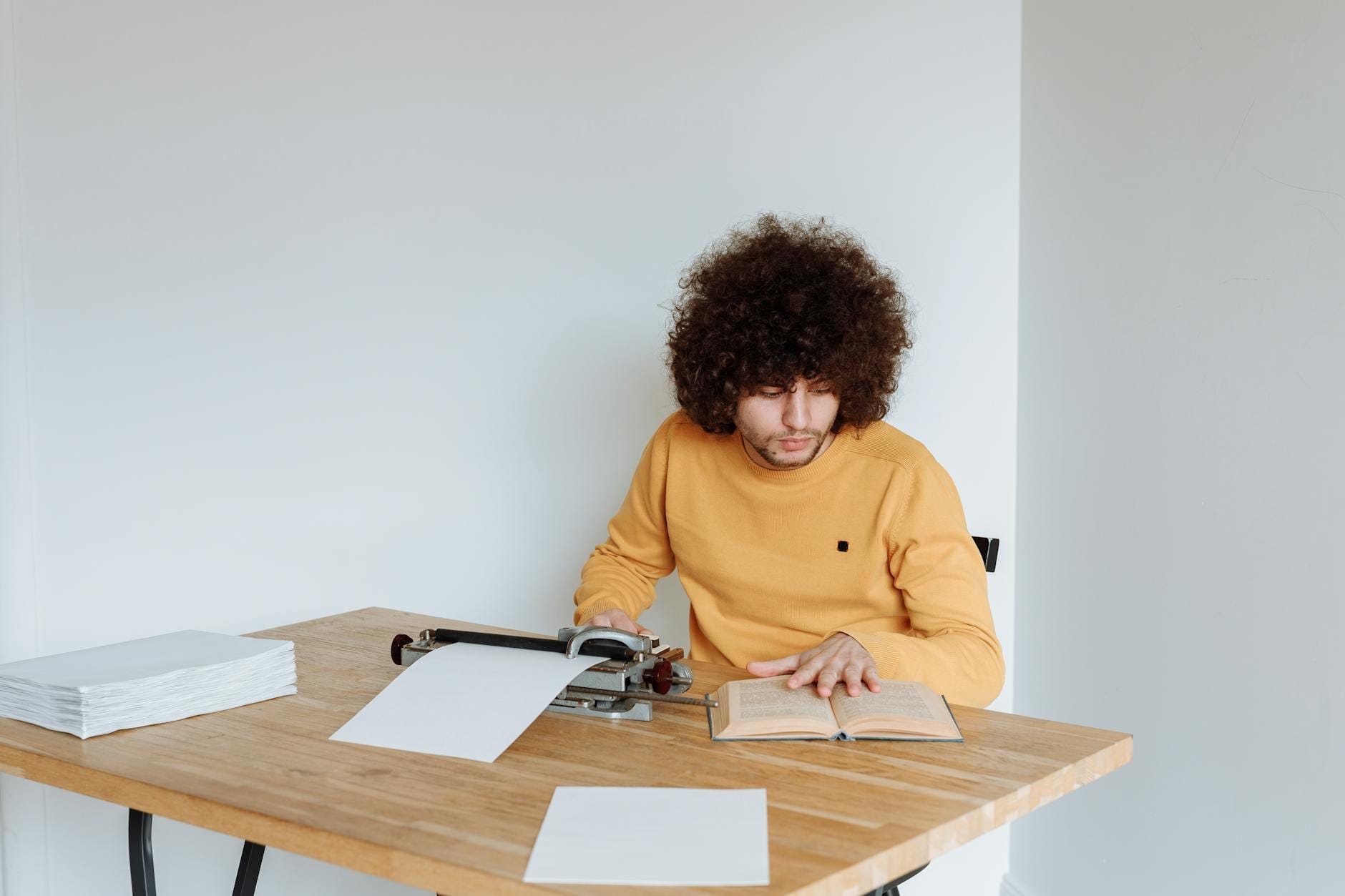 Młoda osoba czyta książkę przy maszynie do pisania przy drewnianym stole