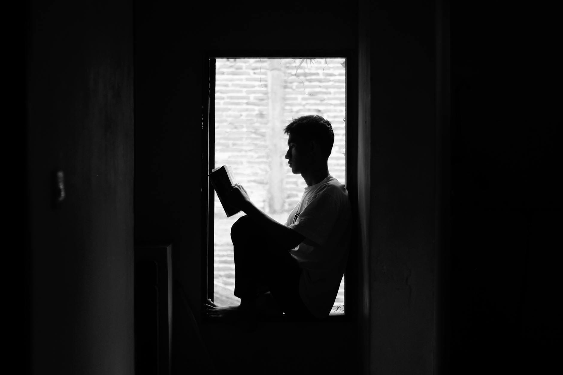 Osoba czytająca książkę przy oknie w czarno-białym kadrze