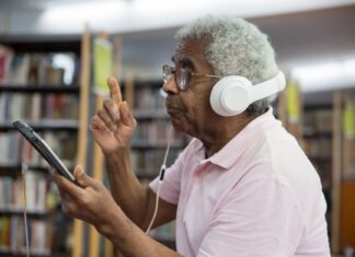 Książka papierowa, e-book czy audiobook: co wybrać do nauki i odpoczynku? Starszy mężczyzna w bibliotece korzystający z tabletu i słuchawek